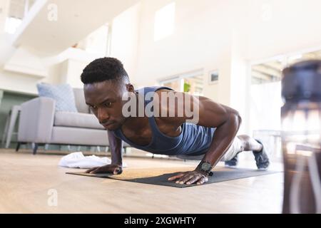 Focused african american man exercising at home, doing push ups. Fitness, training, exercise, domestic life and healthy lifestyle, unaltered. Stock Photo