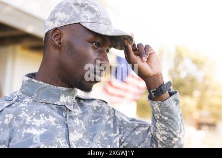 Thoughtful african american male soldier in uniform standing outside home holding peak of cap. Military service, army, home, domestic life and lifesty Stock Photo