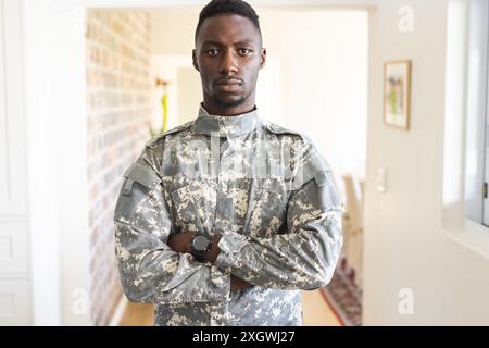 Portrait of serious african american male soldier standing with arms crossed at home, copy space. Depression, ptsd, military service, army, return, ho Stock Photo
