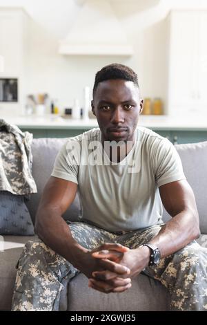Portrait of serious african american male soldier sitting on couch at home. Depression, ptsd, military service, army, return, home, mental health and Stock Photo