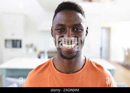 Portrait of happy african american man in sunny kitchen smiling. Wellbeing, domestic life and lifestyle, unaltered. Stock Photo