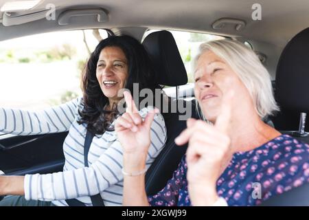 Two happy diverse senior female friends going on road trip smiling and talking in car. Friendship, vacations, road trip, travel and active senior life Stock Photo