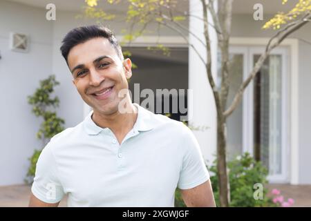 Middle Eastern man stands smiling in a sunny outdoor setting. His casual attire suggests a relaxed day at home or in a community space. Stock Photo