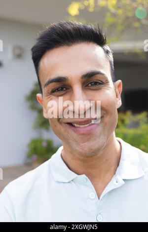 Middle Eastern man smiles warmly outdoors, unaltered. His cheerful expression brightens the sunny, residential setting. Stock Photo