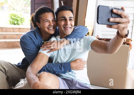 Biracial couple taking a selfie at home, with copy space. They share a joyful moment capturing memories together. Stock Photo