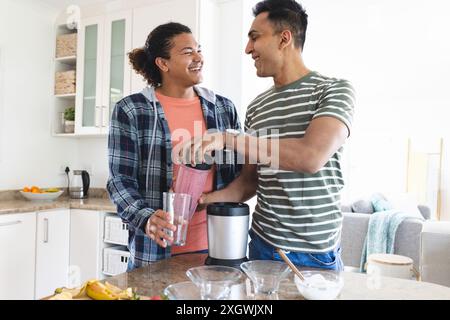 Gay biracial and Middle Eastern couple making smoothies in a home kitchen. They share a joyful moment while preparing a healthy drink together. Stock Photo