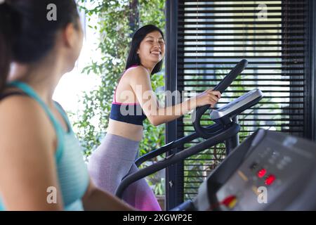 Happy asian female friends wearing sports clothes and exercising at home. Domestic life, friendship, activity and lifestyle, unaltered. Stock Photo