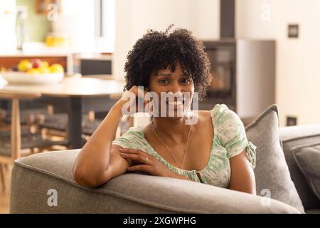 Young biracial woman relaxes on a couch at home, with copy space unaltered. She exudes comfort and ease in a cozy living room setting. Stock Photo