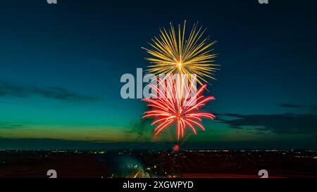 Bright Fireworks Exploding In The Night Sky With Vibrant Red And Yellow Colors Over A Cityscape With Distant Lights, Set Against A Dark Blue And Green Horizon, Capturing A Festive Celebration. Stock Photo
