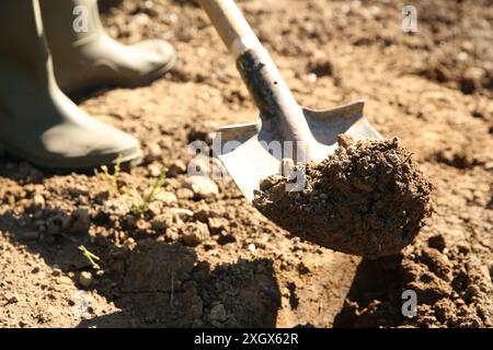 Farmer digging soil with shovel on sunny day, closeup Stock Photo