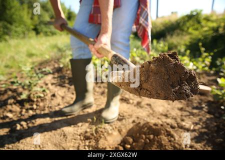 Farmer digging soil with shovel on sunny day, closeup Stock Photo