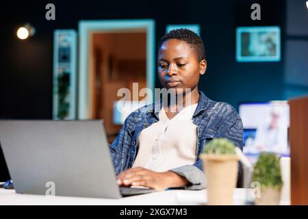 Focused college student working on her thesis, using a laptop for researching, and reviewing information online. Dedicated and determined, black woman working from home on personal computer. Stock Photo