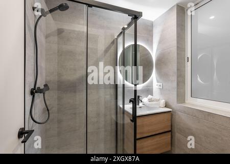 Modern Minimalist Bathroom with Glass Shower, Elegant Round Mirror and Contemporary Design Stock Photo