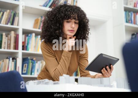 Female architect with city layout using digital tablet at library table with books in background Stock Photo