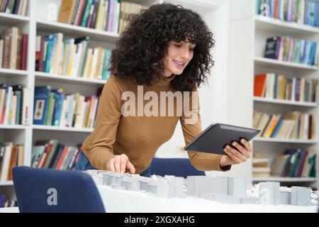 Female architect with city layout using digital tablet at library table with books in background Stock Photo