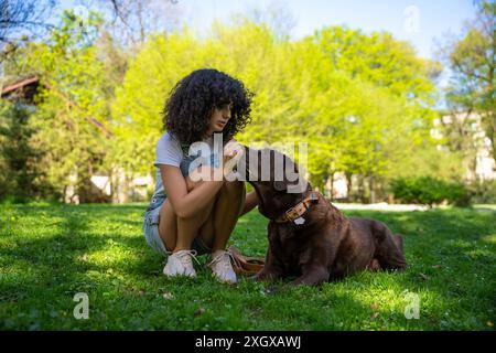 Curly-haired young woman playing with her dog in the park Stock Photo