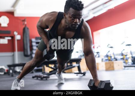 Fit African American man doing dumbbell rows at the gym. His workout routine emphasizes strength and fitness. Stock Photo