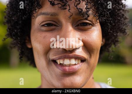 Close-up of a young biracial woman smiling outdoors, with copy space unaltered. Her joyful expression brightens the natural setting around her. Stock Photo