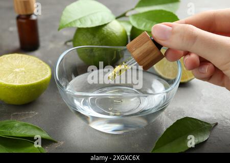 Woman dripping essential oil from pipette into bowl at gray table, closeup Stock Photo