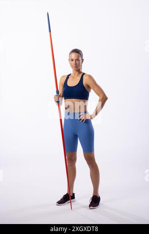 Athletic young Caucasian female athlete poses with a javelin on a white background. She's ready for track and field competition, showcasing strength a Stock Photo
