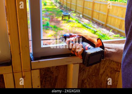 An employee of construction company installs window in new house with help screwdriver Stock Photo