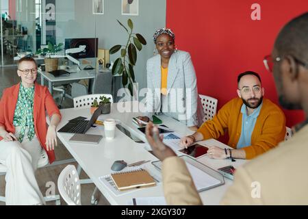 Multi-ethnic team of colleagues collaborating during office meeting, with laptops and documents on table in marketing agency Stock Photo