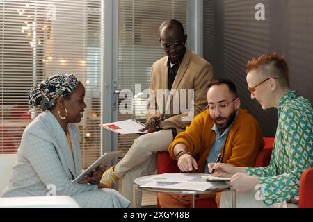 Diverse group of professionals collaborating in office meeting, focusing on reports and discussing future plans in relaxed setting Stock Photo