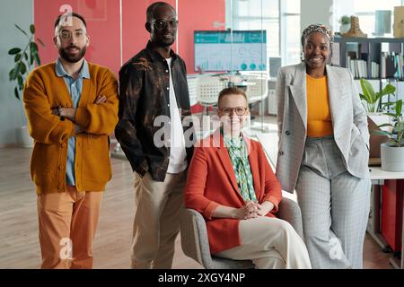 Group of diverse colleagues posing confidently in modern office. Includes Caucasian, Black person, and multiracial members, highlighting teamwork and diversity Stock Photo