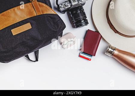 A flat lay with essential travel items such as a backpack, camera, passport, hat, a bottle, and wireless earbuds Stock Photo