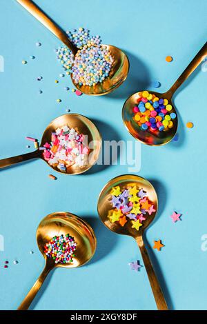 Top view of various colorful sprinkles in round golden spoons against a light blue background Stock Photo