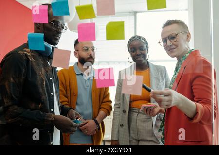 Group of colleagues engaging in creative brainstorming session, using colorful sticky notes on glass wall, sharing and discussing innovative ideas in office Stock Photo