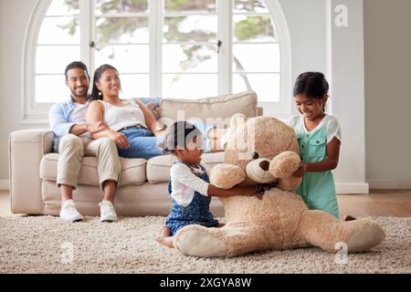 Girl, siblings and playing with teddy bear in home on carpet for bonding, fun activity and fantasy game. Parents, sister and happy with fluffy toy on Stock Photo