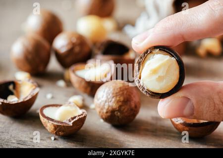 Closeup view of fingers holding Macadamia nut. Macadamia nuts on wooden board in background. Stock Photo