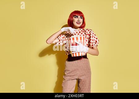 Woman with red hair holding box of popcorn on yellow background in comic-inspired pop art style. Stock Photo