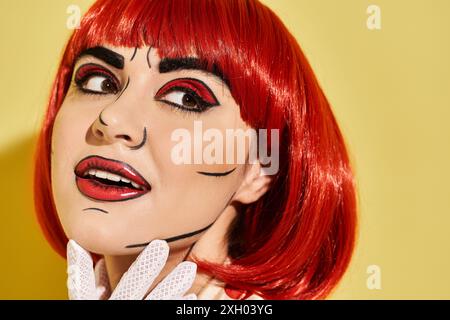 Close-up of a pretty redhead with creative pop art makeup, dressed in a polka dot blouse, set against a yellow background. Stock Photo