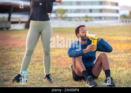 Couple using a social media app on a smartphone while exercising outdoors. Stock Photo