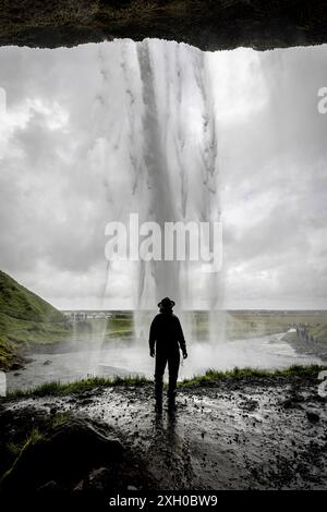 Man is admiring a powerful Seljalandsfoss waterfall in iceland on a cloudy day Stock Photo