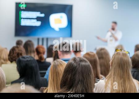 Diverse audience in a business conference listening to a speaker with a presentation displayed on a screen. Stock Photo