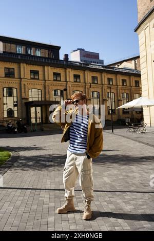 Red-haired man in debonair attire stands in front of building. Stock Photo