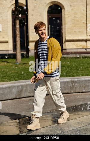 Young man with red hair walks along sidewalk in front of building. Stock Photo