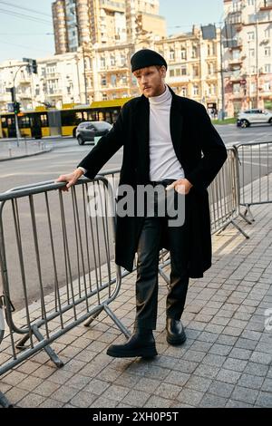 Young red-haired man leaning on fence with hands on hips in urban setting. Stock Photo