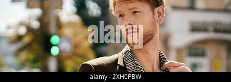 Red-haired man in suave suit standing confidently on city corner. Stock Photo
