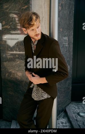 A red-haired man in debonair attire leans against a city pole. Stock Photo
