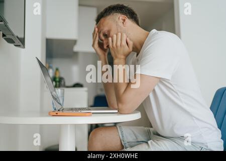 Young man experiencing burnout and stress while working on laptop at home, midlife crisis, mental health issues. Stock Photo
