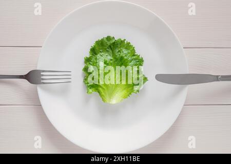 Leaf lettuce on white plate with fork and knife, mono diet for weight loss Stock Photo