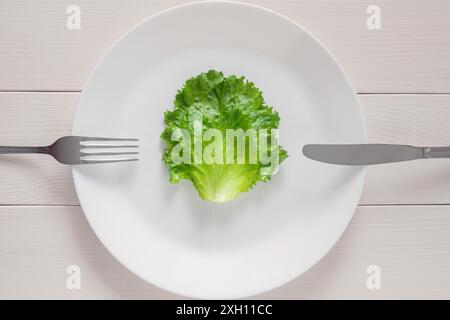 Leaf lettuce on white plate with fork and knife, detox mono diet for weight loss Stock Photo