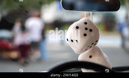 Two white dice hang from the rearview mirror of a car Stock Photo