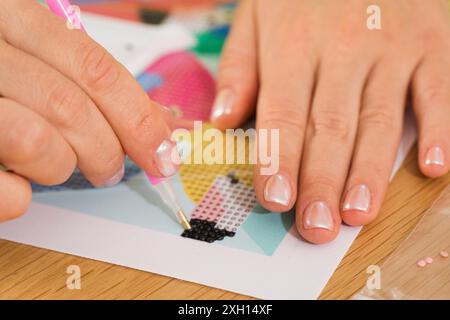 A close-up of a hand placing crystals on a canvas for a diamond painting project. Diamond Mosaic Stock Photo