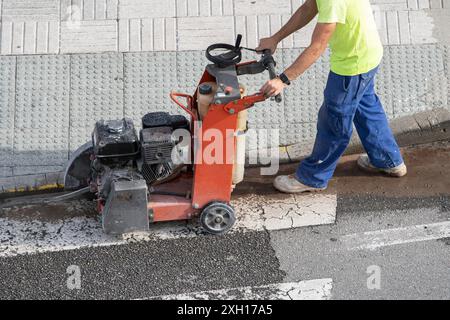 Construction worker cutting concrete floor with diamond saw blade machine on a sidewalk Stock Photo