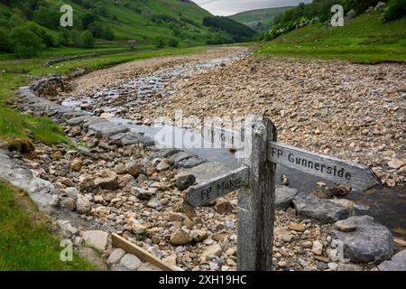 River Swale, picturesque steep-sided hills & fingerpost sign (water flowing, dry summer weather, gravel bed) - Swaledale, Yorkshire Dales, England UK. Stock Photo